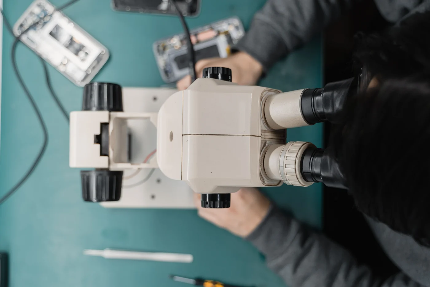 Vista superior de reparo de smartphone sob microscópio, com componentes e ferramentas de precisão