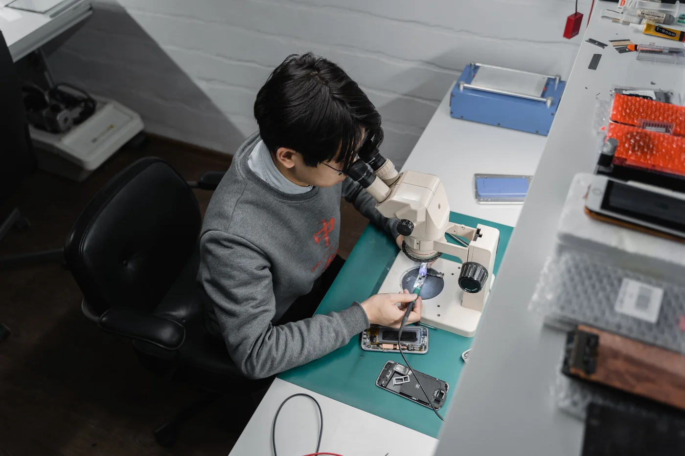 Técnico examinando os componentes de um smartphone com microscópio em bancada de reparo